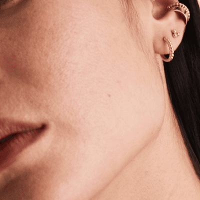close-up of woman's ear with gold beaded hoop earrings, a beaded post earring, and an ear cuff