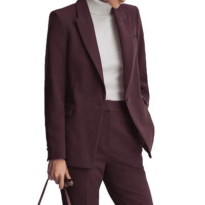 woman wears dark purple/berry pant suit with a beigey turtleneck; she is carrying a handbag