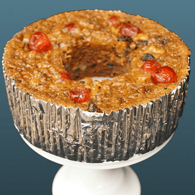 fruitcake in a silver tin sits on white pedestal