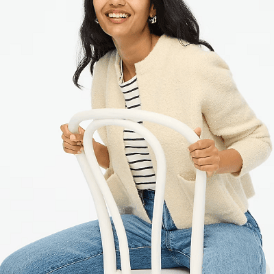 A woman sitting on a chair wearing a cream-colored J.Crew Factory cardigan sweater and jeans