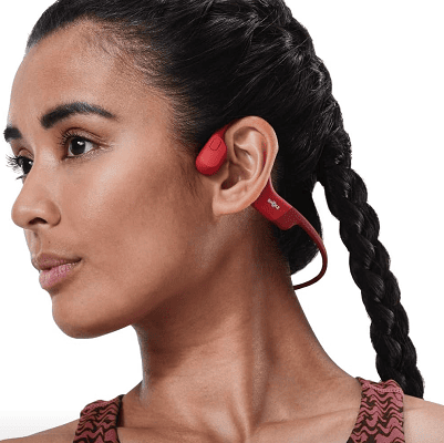 model wears red earbuds that go over the ear and behind the neck; they involve bone conduction