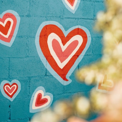 hearts are painted on a blue brick wall; the hearts are blue, red, white, and a lighter red. In the foreground there is a blurry tree or perhaps string lights.
