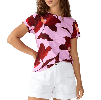 woman wears pink t-shirt with large red flower print on it; some of the flowers have coral and white in the center