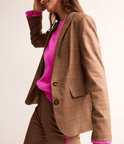 woman wears brown suit with light pink check pattern; she also wears a bright pink sweater