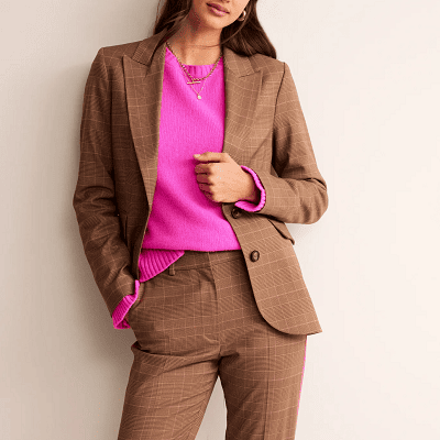 woman wears brown suit with light pink check pattern; she also wears a bright pink sweater