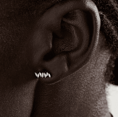 Black model wears diamond earrings in white gold with a zigzag pattern (extreme zoom so only her ear and part of her neck is visible)