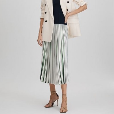 A woman wearing a cream oversized blazer, black top, and mint striped skirt