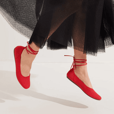 woman wears red flats with wrap-around ankle straps; she is jumping and wearing what looks like a black tulle skirt