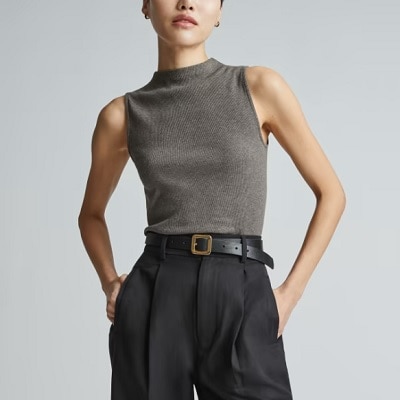 A woman wearing a gray funnel-neck sleeveless tank top and black trouser with belt