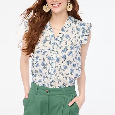 A woman wearing a white and blue floral sleeveless blouse and green pants
