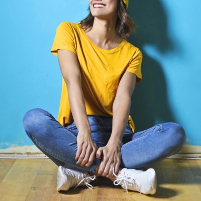 smiling woman wears denim blue jeans with white sneakers and yellow tee