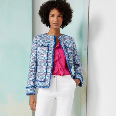 A woman wearing a pink top, white pants, and blue-patterned jacket