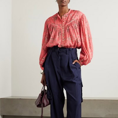 A woman wearing a pink printed long sleeve button blouse and a blue cargo trouser pants and maroon bag