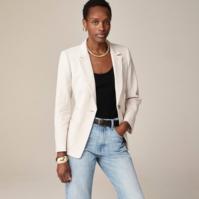 A woman wearing an ivory blazer, black top, light-blue jeans, and gold jewelry