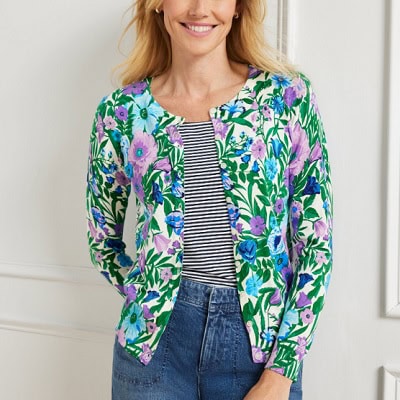 A woman wearing a green flower printed cardigan with black and white stripe top underneath and denim pants
