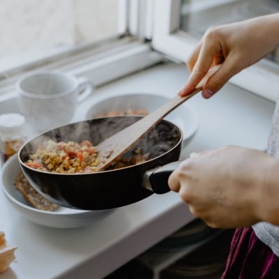 close up of a steaming pan with a rice/veggie dish maybe from one of the best meal kit services; one hand holds the pan while another holds a wooden spoon and serves the dish onto a plate