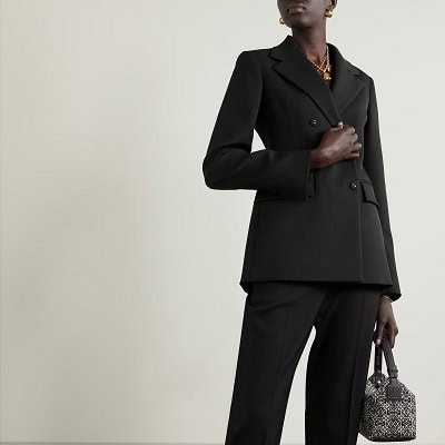 Black woman wears black double-breasted wool twill suit; she carries a small black and white handbag