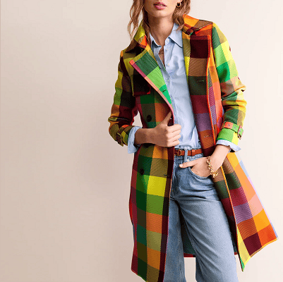 woman wears bright multi-colored trench coat with light blue button up and light blue jeans