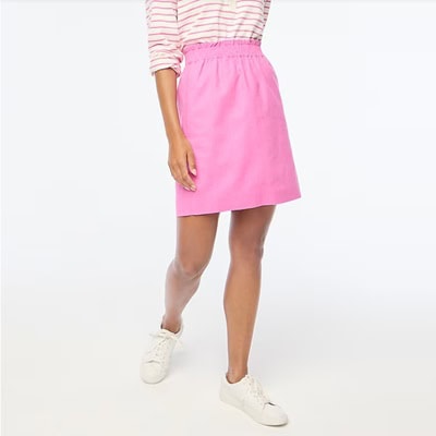 A woman wearing a pink-and-white striped top, a pink skirt, and white sneakers