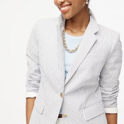 A woman wearing a white and blue stripe blazer and sky blue top inside with gold necklace