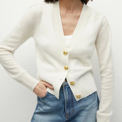 A woman wearing an ivory cardigan, white top, and blue jeans