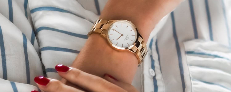 woman wears gold wristwatch; she is also wearing a stripey blouse and has red nails