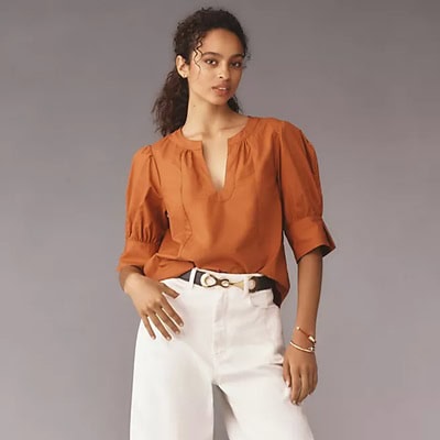 A woman wearing a rust-colored blouse and white pants with a belt