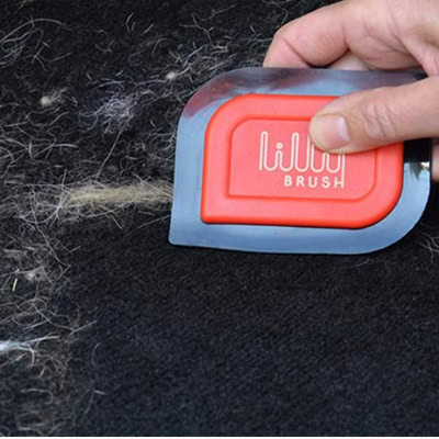 A person's hand holding a red-and-black pet hair remover tool, removing white pet hair from a black surface