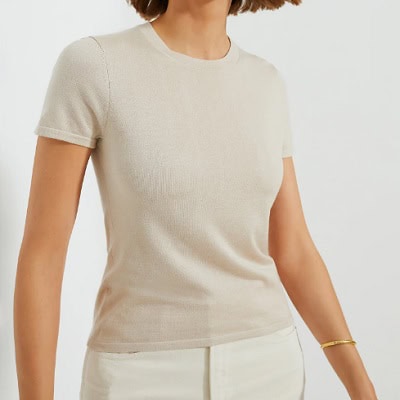 A woman wearing a cashmere tee and white pants with gold bracelet