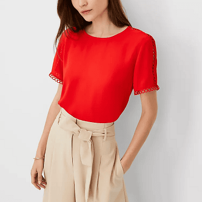 woman wears red blouse with circular trim at the neckline, on the cuffs of the sleeves, and as itty bitty cutouts along the side from the neckline to the cuff