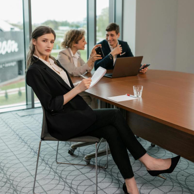 snooty looking woman sits at a conference table with two colleagues; she is wearing a pant suit and wondering what to wear when you work with finance bros
