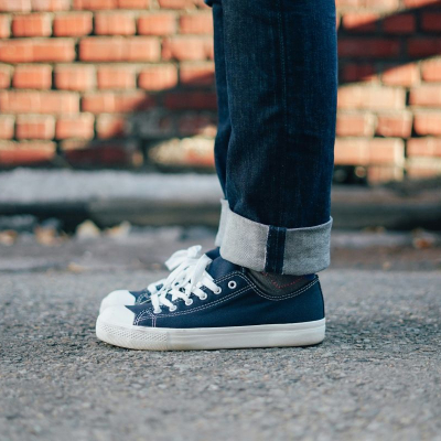 person wears sneakers with blue denim; they are standing in front of a brick wall