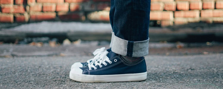 person wears sneakers with blue denim; they are standing in front of a brick wall