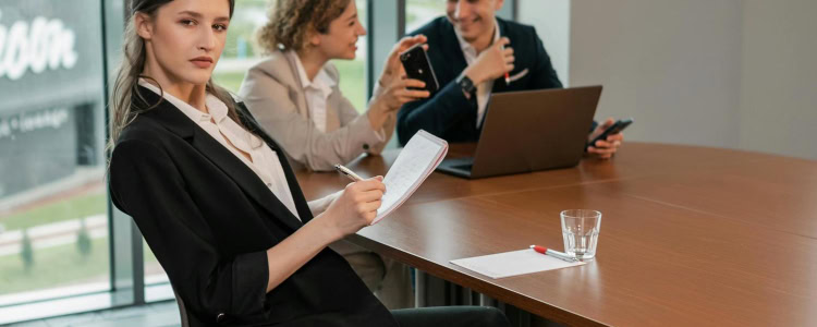 snooty looking woman sits at a conference table with two colleagues; she is wearing a pant suit and wondering what to wear when you work with finance bros