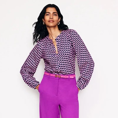 A woman wearing a pink-and-navy print shirt,, a pink belt, and purple pants