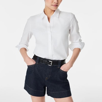 A woman wearing a white long sleeve polo top and denim short with belt