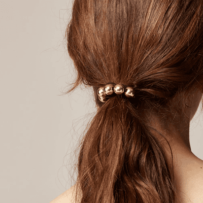 brunette wears hair tie with gold baubles in her ponytail