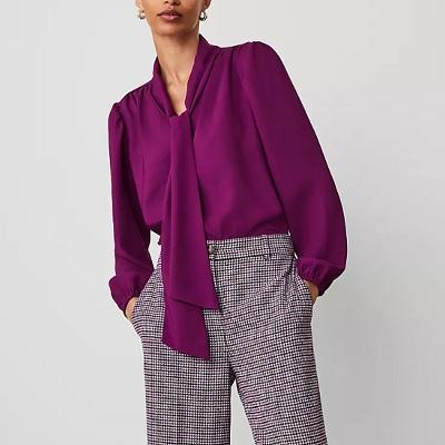 A woman wearing a purple long sleeve tie neck top and trouser pants