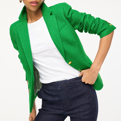 woman wears green tweed blazer, white shirt, and denim pants; her sleeves are scrunched up and she's leaning in a weird way