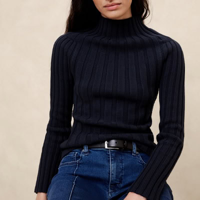 A woman wearing a black turtleneck ribbed sweater and denim pants with black belt