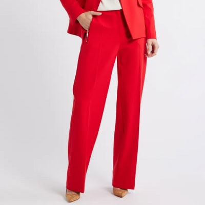 A woman wearing a red blazer with white blouse and red trouser pants with cream pointed shoes