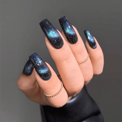 woman has nail polish on with sparkles and sheen that look a bit like the cosmos; she is wearing a ring on her second and fourth fingers, and possibly a leather jacket