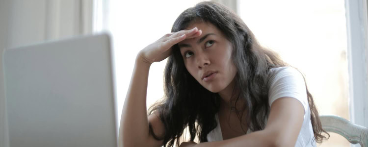 A woman sitting at a desk with a laptop in front of her. She has her hand to her forehead and a disappointed expression.