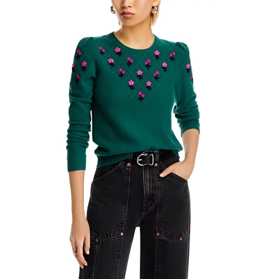 A woman wearing black pants and a green sweater with embroidered pink flowers