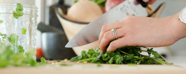 woman chops an herb; there is a bowl of vegetables on the table behind her