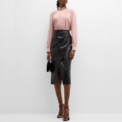 A woman wearing a pink long sleeve top and midi leather skirt with black heels and black small bag