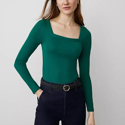 A woman wearing a green long sleeve square neck top and denim pants with black belt