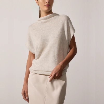 A woman wearing a beige funnel neck top and a skirt