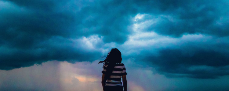 woman in stripey shirt stands looking at dark clouds while wind blows her long hair to the side