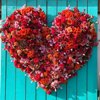 heart made of flowers hangs on a blue wooden slat wall